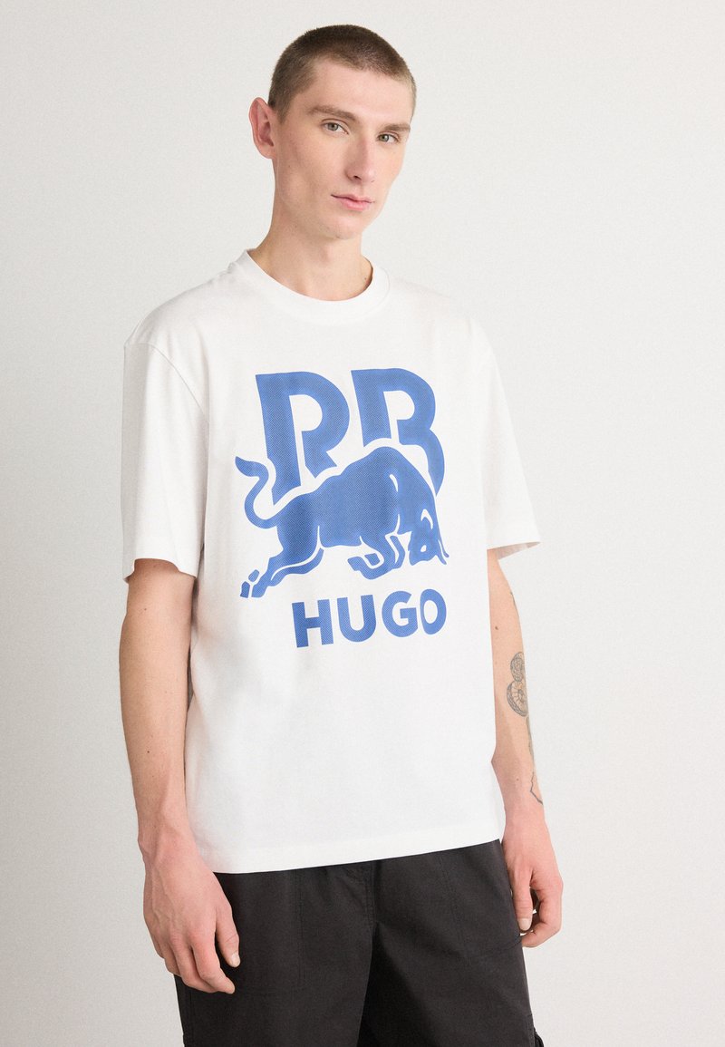 Hvit bomull T-skjorte med et stort blått grafisk motiv av en okse og teksten "RB HUGO." Korte ermer og en avslappet passform.