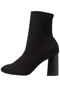 Bottine noire avec une tige en tricot ajustée, un bout pointu et un talon cylindrique épais. Texture lisse avec peu de détails.