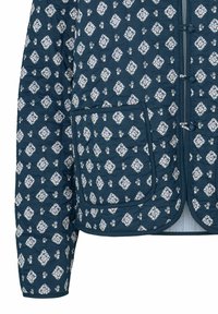 Giacca trapuntata di colore blu navy con motivi a diamante floreali bianchi. Caratterizzata da un colletto rotondo e due tasche frontali con dettagli a bottone.