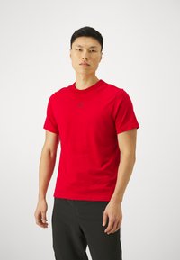 T-shirt atlético vermelho de manga curta, feito de um tecido suave, com um pequeno logo Jumpman preto no peito e decote redondo.