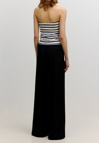 Gestreepte, fitting tube top in crème en marineblauw, gecombineerd met hoogwaardige, wijde zwarte trousers. Soepele stof en ontspannen silhouet.