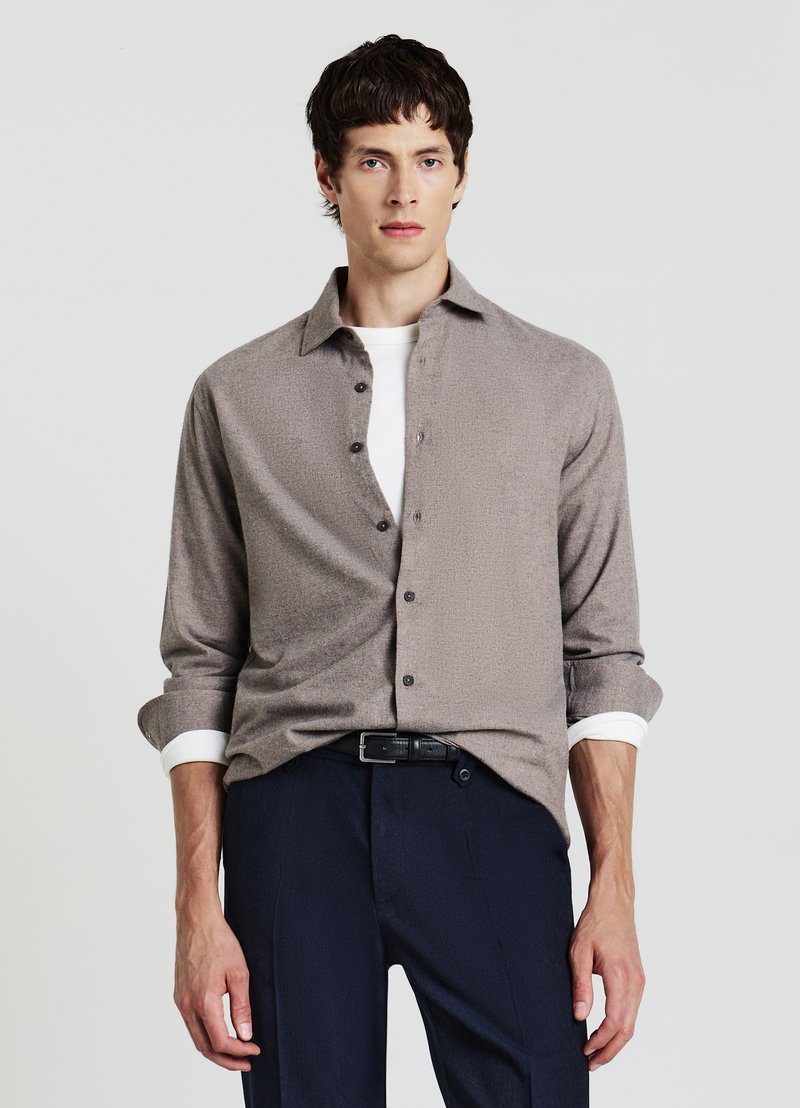 Camicia marrone chiaro con bottoni, motivo strutturato, maniche arrotolate e polsini bianchi, abbinata a pantaloni scuri e cintura nera.