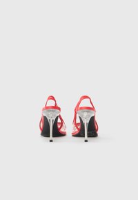 Κόκκινα σανδάλια με ψηλό τακούνι που διαθέτουν διάφανους ιμάντες, κομψό σχεδιασμό και μεταλλικό ασημένιο τακούνι με μαύρη σόλα.