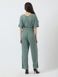 Grønn plisserte jumpsuit med V-rygg, brede ermer og knyttet midje. Kombinert med svarte høye hæler. Loddrett tekstur over hele antrekket.