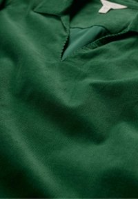 Polo verde realizzato in tessuto morbido, con un corto pattina e colletto. La texture è liscia con una leggera lucentezza.