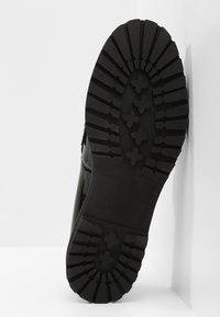 Semelle en caoutchouc noir avec des rainures profondes et des motifs croisés ; présente une tige noire lisse, une construction solide et un design à bout arrondi.
