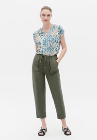 Kurzarmoberteil mit V-Ausschnitt und mehrfarbigem abstrakten Druck; olivgrüne, lässig sitzende Hose mit vorderen Taschen und verstellbarem Kordelzugbund.
