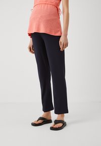 Koralen, kratka majica s kratkimi rokavi in vrvico v pasu; v kombinaciji z mornarsko modrimi, ohlapnimi hlačami in črnimi japonkami. Preprost, vsakdanji outfit.