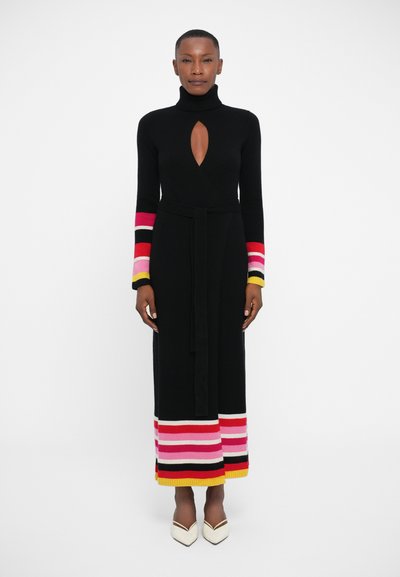 Sort strikkjole med en mock neck, der har en nøglehulskæring og multicolor stribede ærmer og kant, der er knyttet om taljen.