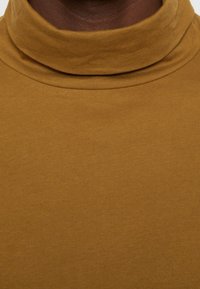 Senfgelber Rollkragenpullover aus weichem, dehnbarem Stoff mit glatter Textur und eng anliegendem Design.