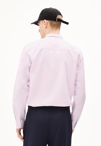 Lange mouwen lavendel shirt met een rechte snit, geknoopte manchetten en een rug yoke detail, gecombineerd met een zwarte pet en donkere broeken.