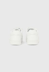 Λευκά αθλητικά παπούτσια με λείο δερμάτινο φινίρισμα, σχεδιασμό χαμηλού προφίλ, στρογγυλή μύτη και επενδεδυμένο γιακά. Ορατά κορδόνια και ελάχιστες λεπτομέρειες σήμανσης.