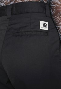 Black fabric pants featuring a back pocket, sleek design, and a white square label with a logo on the right side.