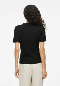 Top nero a maniche corte con finitura testurizzata, collo a giro e leggero dettaglio a scallop nella parte posteriore, abbinato a pantaloni di colore chiaro.