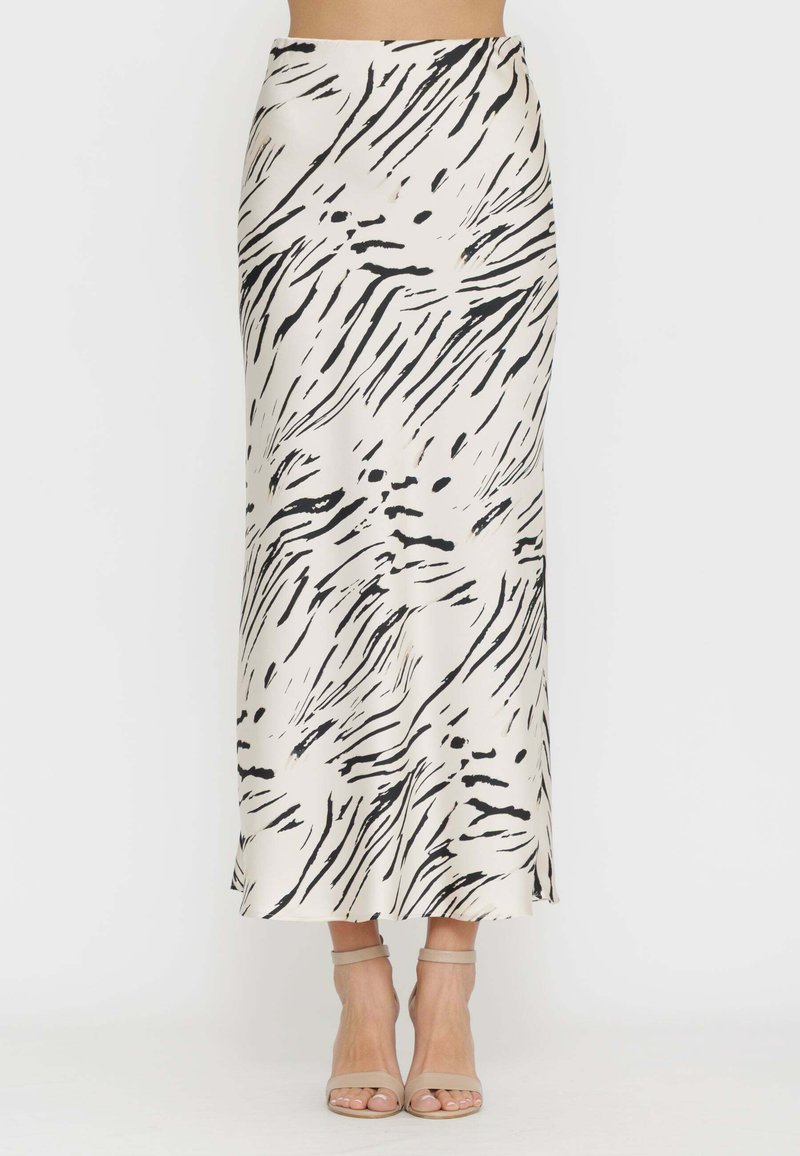 Donna che indossa una gonna in satin a vita alta, lunga fino alla caviglia, con stampa astratta a zebra bianca e nera, e tacchi nude con cinturino alla caviglia.