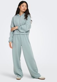 Survêtement bleu clair à coupe décontractée avec veste à capuche zippée et pantalon à jambes larges. Tissu doux avec poignets et taille élastiques. Design décontracté.