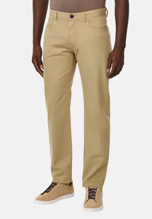 Pantaloni di cotone beige con design a gamba dritta, dotati di chiusura a bottone, tasche anteriori e sottili dettagli di cucitura. Abbinati a scarpe marroni.