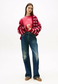 Cárdigan a rayas rojas y rosas sobre una camiseta rosa, combinado con unos vaqueros de tiro ancho de color azul y unos zapatos marrones de tipo slip-on.