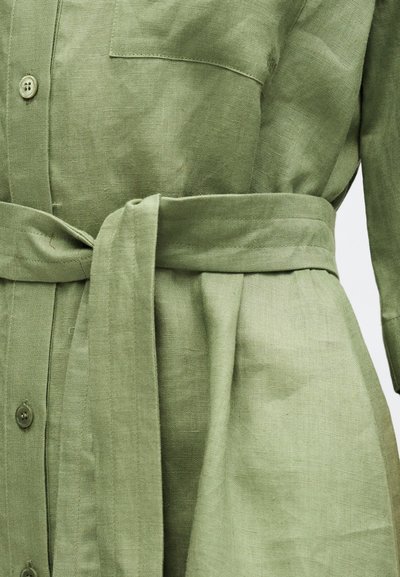 Φόρεμα από λιτό λινό σε ανοιχτό πράσινο χρώμα με κουμπιά μπροστά, τσέπη στο στήθος και ζώνη από το ίδιο ύφασμα δεμένη στη μέση.