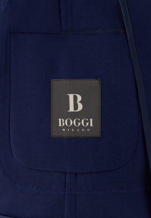 Donkerblauwe stoffen zak met een zwart label waarop in witte tekst "B BOGGI MILANO" staat, vastgestikt op de zak.