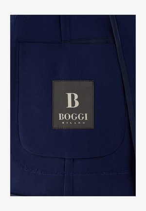 Dunkelblaues Stofftasche mit einem schwarzen Etikett, auf dem in weißer Schrift "B BOGGI MILANO" steht, auf die Tasche genäht.