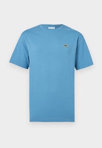 T-shirt bleu uni à manches courtes et col rond avec un petit logo crocodile vert sur la poitrine gauche.