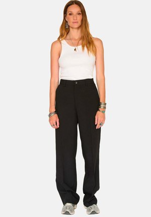 Pantalons larges noirs avec une fermeture à boutons, présentant une coupe ajustée et un tissu lisse. Associés à un débardeur blanc et des baskets grises.