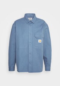 Lichtblauw overhemd met knopen, gemaakt van denimstof. Beschikt over een borstzak met een logo-patch, lange mouwen en een klassieke kraag.