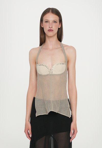 Beige halter top with a fitted bust, adorned with silver studs along the neckline. Lightweight, sheer fabric with a slightly longer hem.