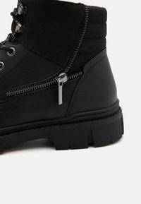 Botas negras hasta el tobillo hechas de cuero y ante, con una suela gruesa y texturizada, ojales, cremalleras y detalles de costura para un diseño adicional.