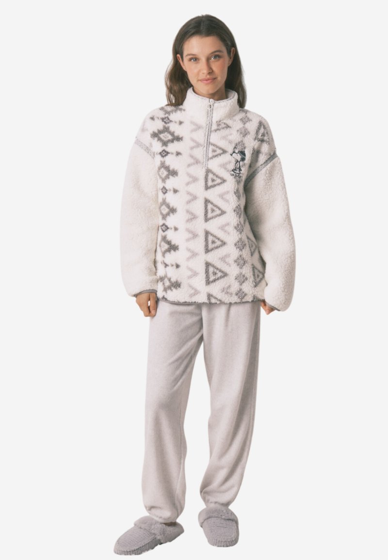 Biały polarowy szerokość z szarymi geometrycznymi wzorami, z pół-zipem, zestawiony z jasnoszarymi spodniami i pasującymi kapciami.