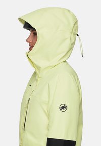 Gelbe wasserdichte Jacke mit Kapuze, ausgestattet mit einem schwarzen Logo am Ärmel und einer verstellbaren Kordel am Hals für einen sicheren Sitz.