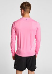 Maglietta sportiva a maniche lunghe di colore rosa, realizzata in tessuto liscio, con scollatura a girocollo e dettagli neri sulle spalle. Pantaloni corti neri visibili sotto.