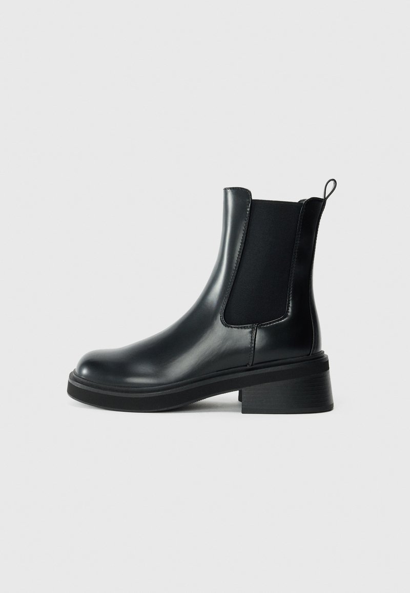 Botte Chelsea en cuir noir avec panneaux latéraux élastiques, bout arrondi et talon carré bas. Finition lisse, avec une languette pour un enfilage facile.