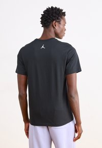 Schwarzes Kurzarm-T-Shirt aus Baumwolle mit glatter Textur und einem weißen Jordan-Logo auf dem Rücken in der Nähe des Kragens.