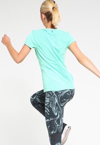Camiseta atlética ligera de color verde menta con mangas cortas, combinada con leggins negros con un patrón azul en espiral.