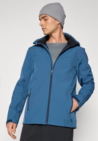 Blue softshell jacket with a front zipper, two side pockets, and a hood. Fabric appears smooth with a slightly textured interior.