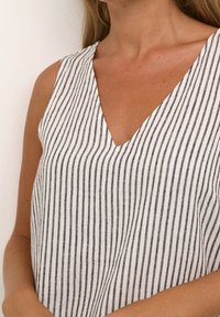 Top sans manches en tissu léger avec des rayures verticales noires et blanches, offrant une coupe décontractée et une finition légèrement texturée.