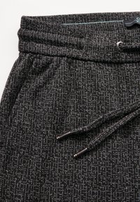Černé joggery s vzorem a texturovanou látkou, vybavené elastickým pasem a šňůrkou na stažení. Stříbrné koncovky na šňůrce.