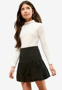Jupe noire évasée avec un ourlet volanté, associée à un col roulé blanc ajusté en maille côtelée. Tissu lisse, design structuré, coupe décontractée.