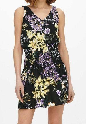 Czarna sukienka bez rękawów z żółto-fioletowymi kwiatowymi wzorami, dekoltem w serek i marszczonym talią, noszona przez stojącą osobę na białym tle.