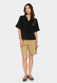 Top nero intrecciato con scollatura a V e maniche corte a campana, abbinato a pantaloni corti color khaki. Presenta una vestibilità comoda e una texture liscia.