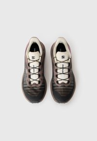 Brune og svarte joggesko med mesh-overdel, hvite detaljer og reflekterende striper. Har robust såle og snøring for en sikker passform.