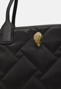 Czarna pikowana torba tote wykonana z gładkiego materiału, z akcentem w kształcie ptaka w kolorze złotym z ozdobnymi detalami.