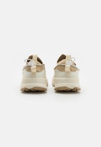 Zapatillas ligeras beige con parte superior de malla, talón texturizado, cordones elásticos y suela de goma duradera. Marca sutil en el talón.