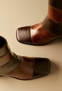 Bottes basses en cuir marron avec un bout carré, présentant une combinaison de panneaux marron foncé et clair et des accents de coutures visibles.