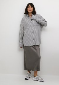 Chemise à rayures grises, coupe oversized, en tissu léger, avec poche poitrine. Jupe en satin gris doux, texture lisse, assortie à des baskets blanches et grises.