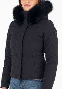 Chaqueta de invierno negra con un cuello de pelaje sintético, bolsillos con cremallera y un diseño ajustado. Tela suave y una silueta moderna.