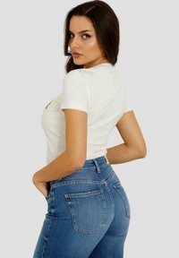 Chemise blanche à manches courtes et jean bleu taille haute. La chemise présente un emblème sur le devant et un design classique en denim à cinq poches.