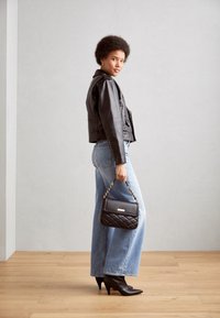 Veste en cuir noire crop, jean taille haute bleu clair, sac à main noir matelassé avec bandoulière en chaîne, et bottes noires à talons aiguilles.